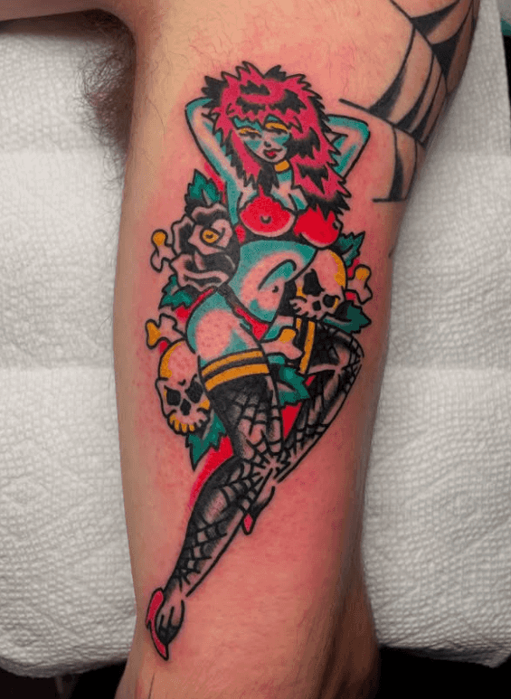 A bright tattoo of a woman in lingerie on a bed of flowers and skulls.