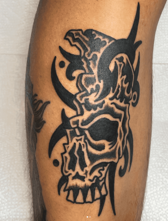 Black and white tattoo of a broken skull.